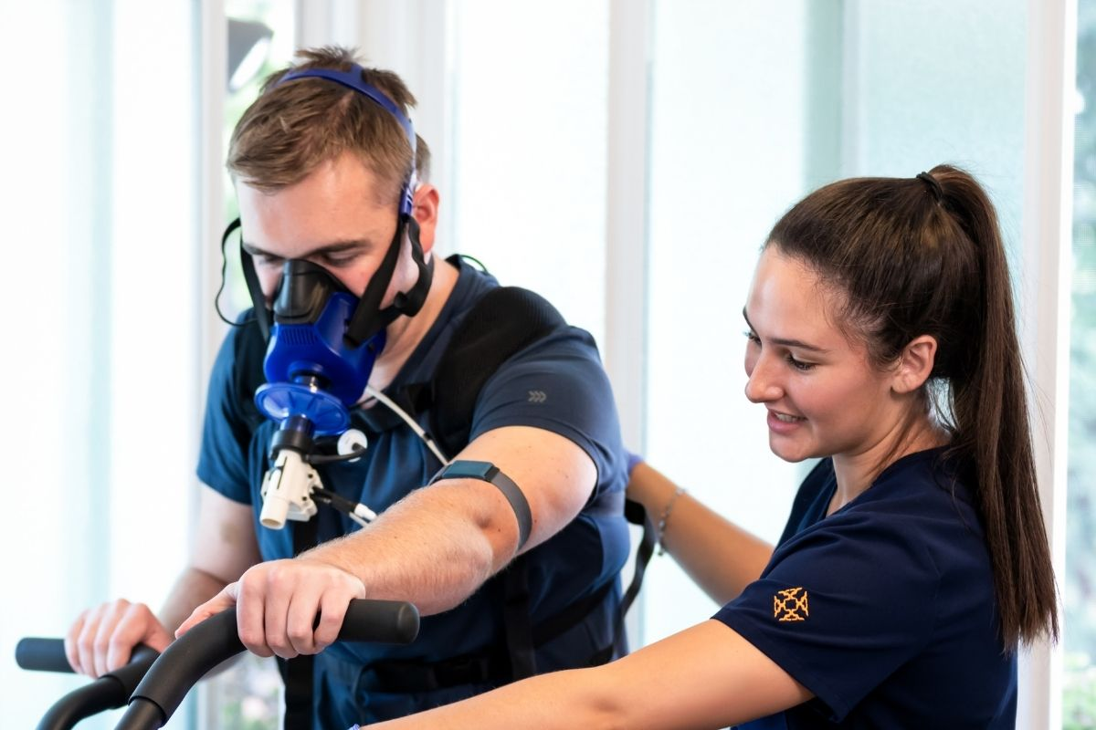 A patient on a bike during VO2 max testing with a YNC team member